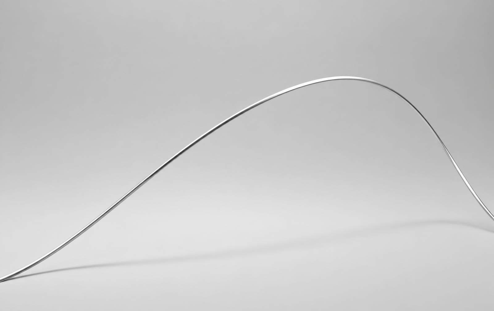 A single polished silver arc rising across a soft grey studio backdrop
